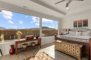 Bedroom with wood finish floors, a ceiling fan, a tray ceiling, and a mountain view