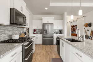Kitchen with stainless steel appliances, light wood-style floors, white cabinets, and light stone counters