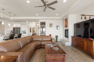 Living area featuring light wood-type flooring, a ceiling fan, a large fireplace, beverage cooler, and recessed lighting