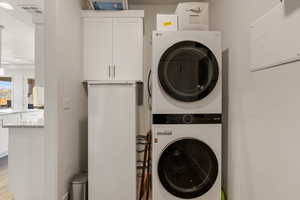 Laundry area featuring stacked washer / drying machine, cabinet space, and light wood-style floors