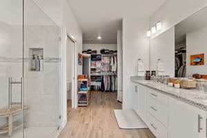 Bathroom with a walk in closet, light wood-style flooring, double vanity, and a stall shower