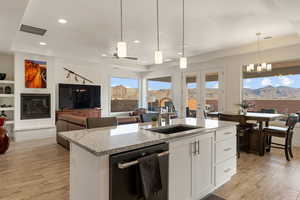 Kitchen featuring open floor plan, light stone countertops, white cabinets, dishwasher, and a kitchen island with sink