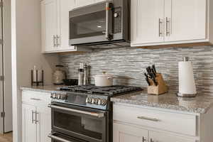 Kitchen with stainless steel appliances, white cabinets, decorative backsplash, and light stone counters