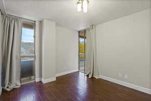 Unfurnished room with dark wood-style flooring, a wall of windows, and a textured ceiling