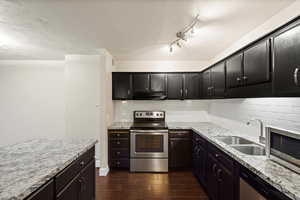Kitchen with stainless steel appliances, decorative backsplash, light stone countertops, and wood tiled floors