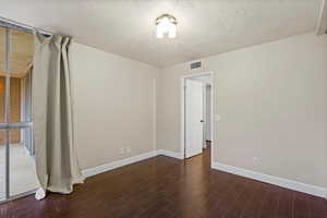 Empty room with dark wood-type flooring and a textured ceiling