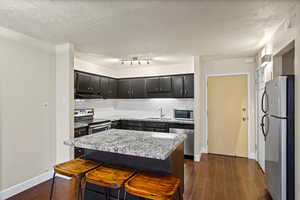 Kitchen with dark cabinets, backsplash, a breakfast bar area, appliances with stainless steel finishes, and a textured ceiling
