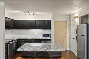 Kitchen with appliances with stainless steel finishes, dark cabinets, dark wood-style floors, backsplash, and light stone countertops
