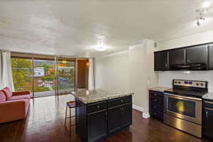Kitchen featuring stainless steel range with electric cooktop, expansive windows, dark cabinetry, a kitchen breakfast bar, and dark wood-style floors