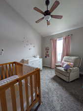 Carpeted bedroom featuring a crib, lofted ceiling, and a ceiling fan