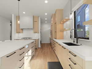 Kitchen featuring light brown cabinetry, decorative backsplash, light wood finished floors, hanging light fixtures, and modern cabinets