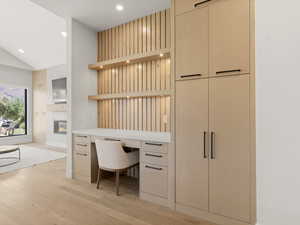 Home office with built in desk, light wood-style floors, recessed lighting, a glass covered fireplace, and vaulted ceiling