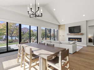 Dining space featuring light wood finished floors, high vaulted ceiling, recessed lighting, a glass covered fireplace, and a chandelier