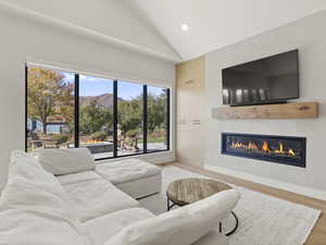 Living area with vaulted ceiling, light wood finished floors, recessed lighting, and a glass covered fireplace