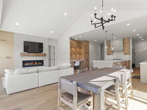 Dining space with light wood-type flooring, recessed lighting, a glass covered fireplace, a chandelier, and high vaulted ceiling