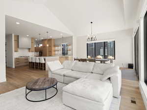 Living area with a chandelier, light wood-type flooring, high vaulted ceiling, and recessed lighting