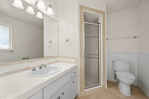 Bathroom with a stall shower, vanity, light tile patterned flooring, and a wainscoted wall