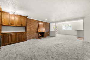 Unfurnished living room featuring a brick fireplace, light carpet, a textured ceiling, and crown molding