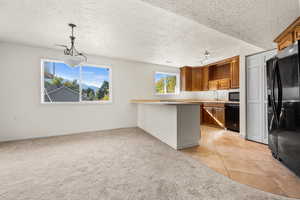 Kitchen with brown cabinets, light colored carpet, light countertops, black appliances, and a textured ceiling