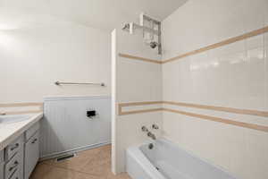 Bathroom featuring bathing tub / shower combination, vanity, a wainscoted wall, and light tile patterned flooring