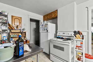 Kitchen with white appliances, a textured ceiling, and light tile patterned flooring