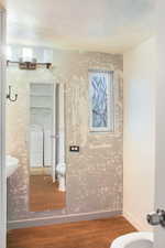 Bathroom featuring dark wood-type flooring, wallpapered walls, and washer and dryer