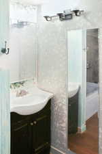 Full bathroom with vanity, dark wood-type flooring, and wallpapered walls