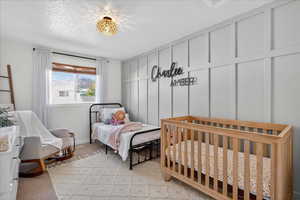 Bedroom with a textured ceiling, light carpet, and a decorative wall