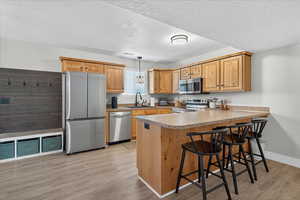 Kitchen with appliances with stainless steel finishes, a textured ceiling, light wood-type flooring, a breakfast bar area, and a peninsula