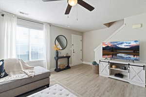 Living room with a textured ceiling, light wood-style floors, and ceiling fan