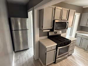 Kitchen with stainless steel appliances, gray cabinets, light countertops, and light wood-style flooring