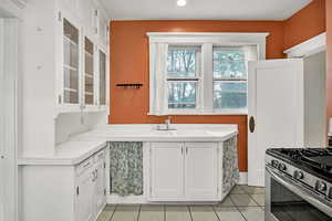 Kitchen with white cabinets, stainless steel gas range oven, light tile patterned floors, light countertops, and glass insert cabinets