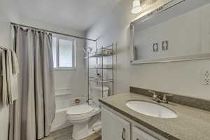Full bath with shower / bath combo with shower curtain, vanity, and light wood-style flooring