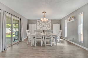 Dining space with healthy amount of natural light, light wood-style flooring, a chandelier, wood walls, and a textured ceiling