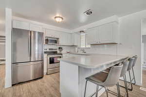 Kitchen with appliances with stainless steel finishes, light countertops, a breakfast bar, a peninsula, and light wood finished floors