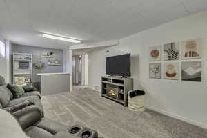 Carpeted living room with a glass covered fireplace and baseboards