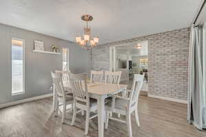 Dining space with light wood finished floors, brick wall, a chandelier, and a textured ceiling