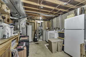 Unfinished basement with freestanding refrigerator, gas water heater, washing machine and clothes dryer, and heating unit