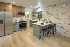 Kitchen with stainless steel appliances, open shelves, a peninsula, a kitchen breakfast bar, and light wood-style flooring
