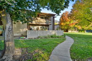 Back of property featuring a balcony, a yard, and stucco siding