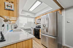 Kitchen featuring light wood-type flooring, light stone countertops, light brown cabinetry, and a raised ceiling
