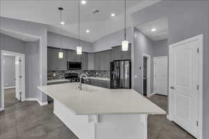 Kitchen with stainless steel appliances, gray cabinets, a kitchen island with sink, a breakfast bar area, and decorative light fixtures
