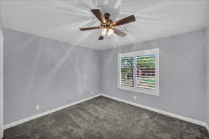 Empty room featuring dark carpet and ceiling fan