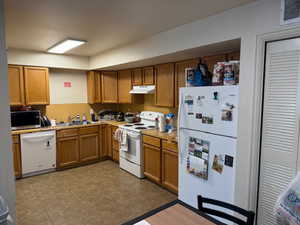 Kitchen with white appliances, brown cabinets, light countertops, and under cabinet range hood