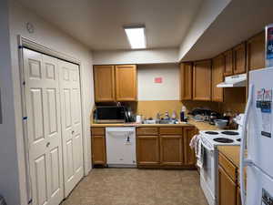 Kitchen with white appliances, brown cabinets, light tile patterned floors, light countertops, and under cabinet range hood