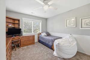 Bedroom featuring light colored carpet, ceiling fan, and built in desk
