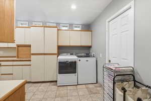 Laundry area featuring cabinet space, light tile patterned floors, and washer and dryer