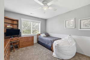 Bedroom featuring an office area, light colored carpet, and a ceiling fan
