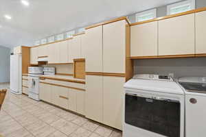 Kitchen with white appliances, light tile patterned floors, light countertops, under cabinet range hood, and washer and clothes dryer
