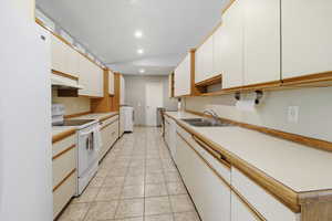 Kitchen featuring white appliances, light countertops, white cabinetry, under cabinet range hood, and light tile patterned floors